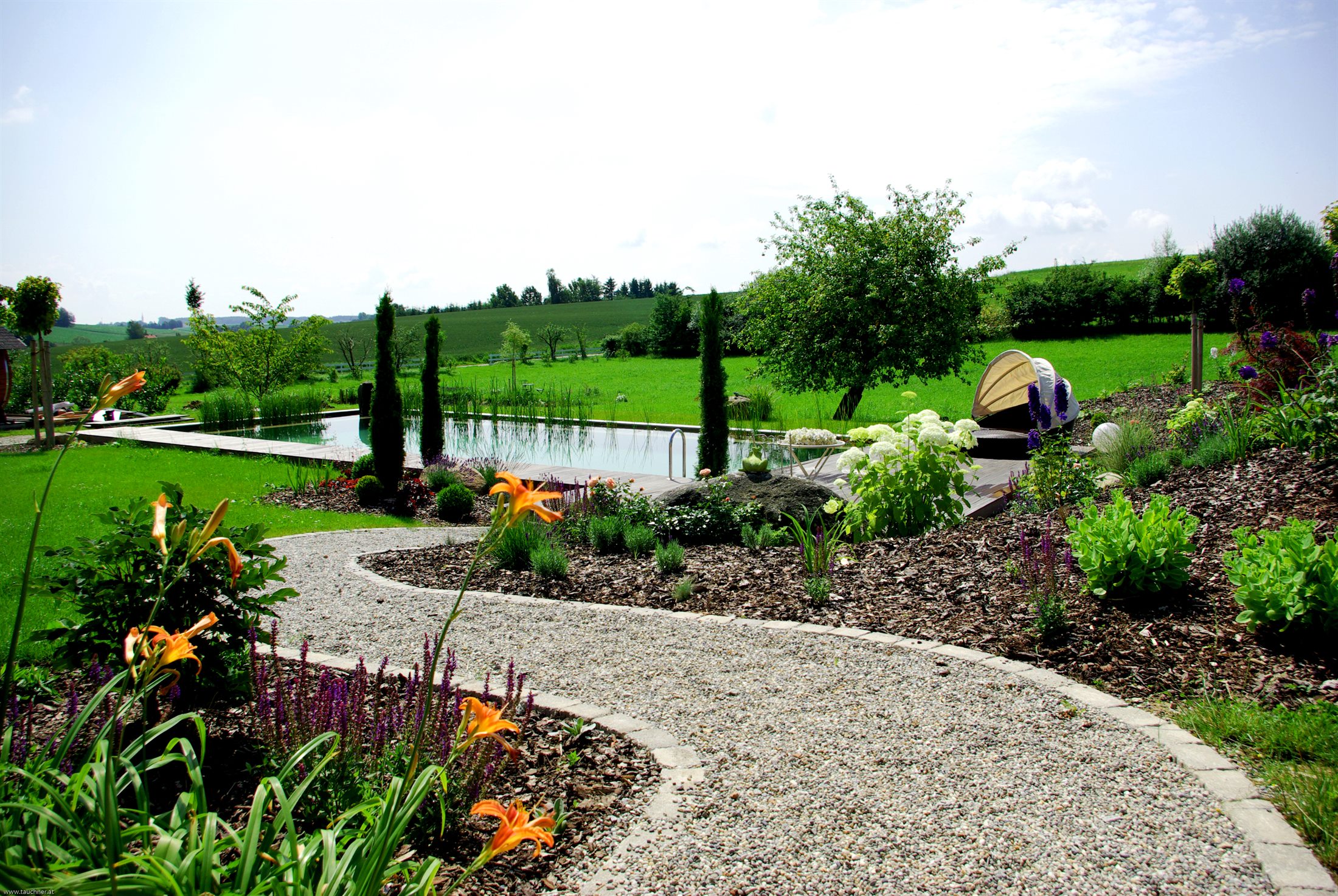 Naturpool in einem grossen Garten mit Blueten und Holzdeck